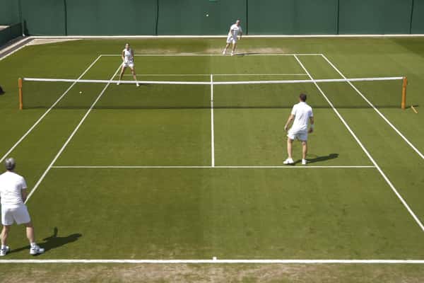 Four players playing tennis on a green grass court at St George's Hill Lawn Tennis Club clinic session.