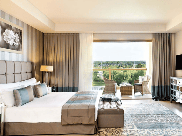 Interior of Sani Beach Deluxe One Bedroom Family Suite with large bed, modern furnishings, and a private balcony overlooking the sea.