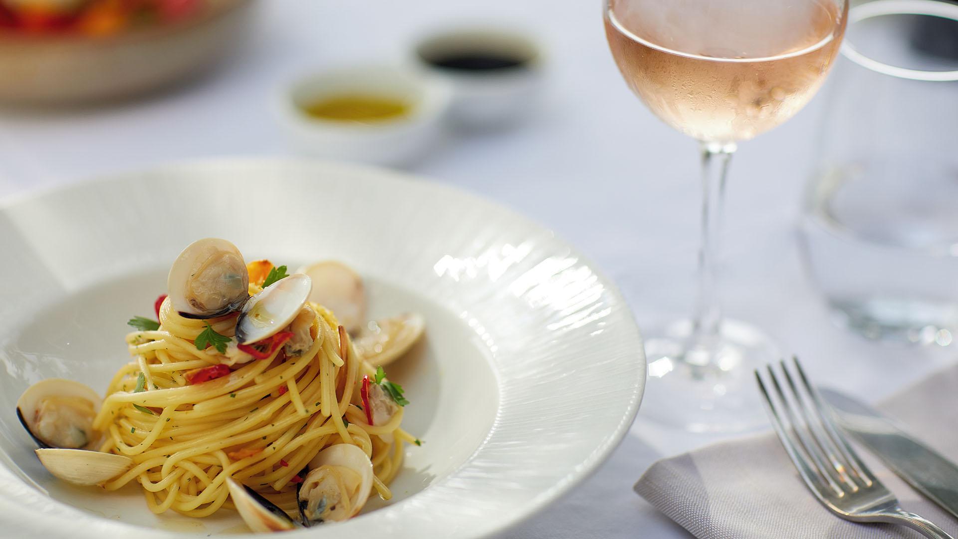 Plate of spaghetti with clams and a glass of rosé wine at Sani Beach dining setup, with olive oil and vinegar in the background.