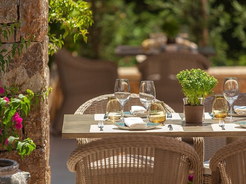 Table at Ammos Restaurant in Sani Beach with glassware, wicker chairs, and a potted herb centrepiece in an outdoor setting.