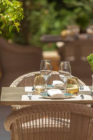 Table at Ammos Restaurant in Sani Beach with glassware, wicker chairs, and a potted herb centrepiece in an outdoor setting.