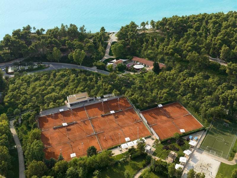 Aerial view of Sani Beach tennis courts surrounded by trees and near the Aegean Sea.