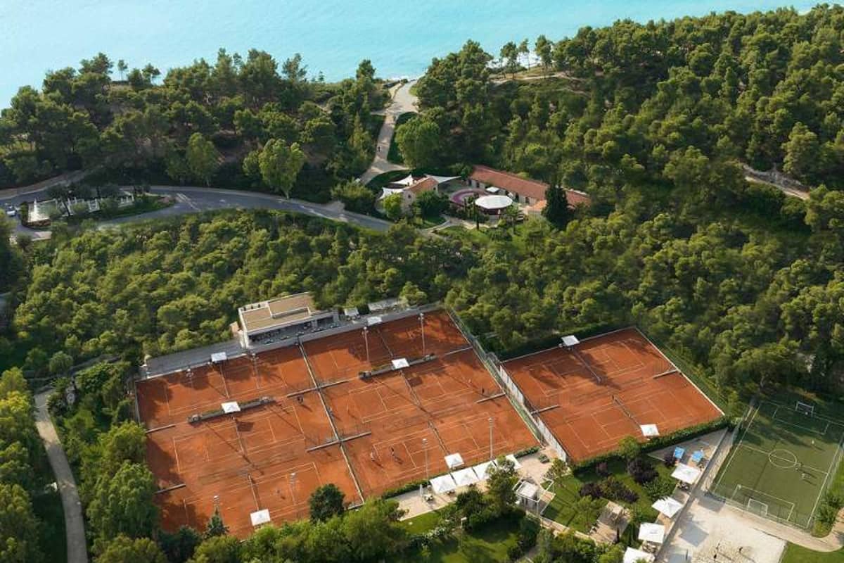 Aerial view of Sani Beach tennis courts surrounded by trees and near the Aegean Sea.