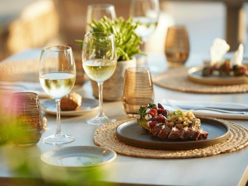 Gourmet dish with grilled meat and herbs on a table set for dining, featuring wine glasses and elegant decor at Sani Beach.