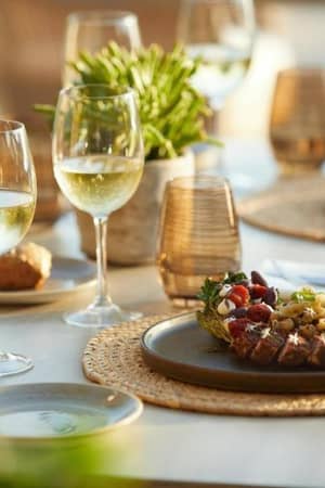 Gourmet dish with grilled meat and herbs on a table set for dining, featuring wine glasses and elegant decor at Sani Beach.