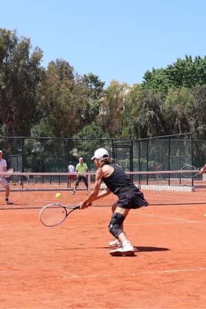 Tennis players on a red clay court at Sani Beach Resort with trees and buildings in the background.