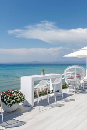 Outdoor seating at Sani Beach Resort, with white tables and umbrellas overlooking the turquoise sea.