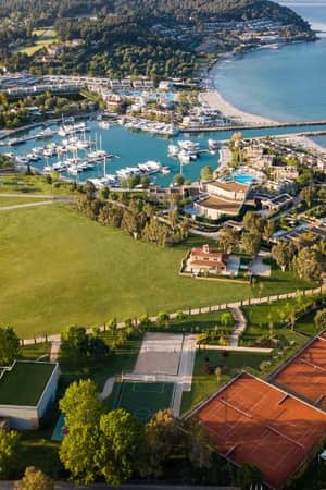 Aerial view of Sani Resort, Halkidiki, featuring a marina, sandy beach, tennis courts, and lush landscapes by the Aegean Sea.