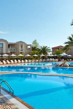 Luxurious outdoor pool at Sani Beach with sun loungers, palm trees, and modern buildings in the background.