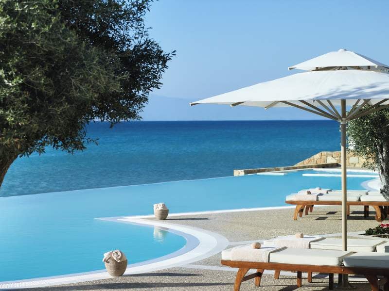 Infinity pool at Sani Beach with sun loungers, umbrellas, and a view of the sea and sky.