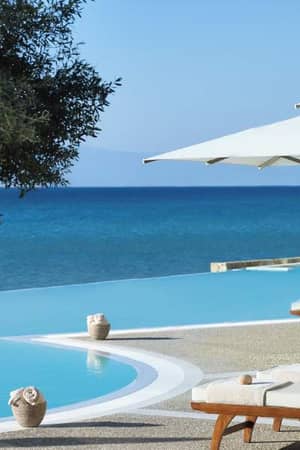 Infinity pool at Sani Beach with sun loungers, umbrellas, and a view of the sea and sky.