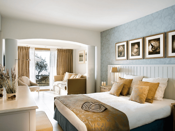 Interior of Sani Beach Junior Suite with a double bed, decorative cushions, seating area, and view of the garden through large windows.