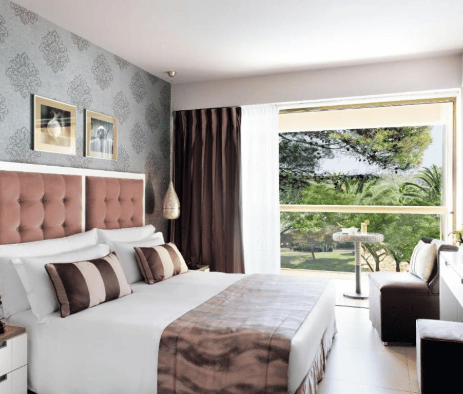 Twin room at Sani Beach with plush bedding and a large window offering a garden view.
