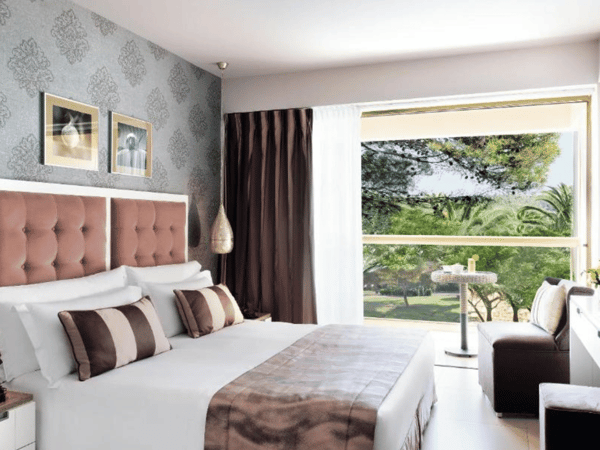 Twin room at Sani Beach with plush bedding and a large window offering a garden view.