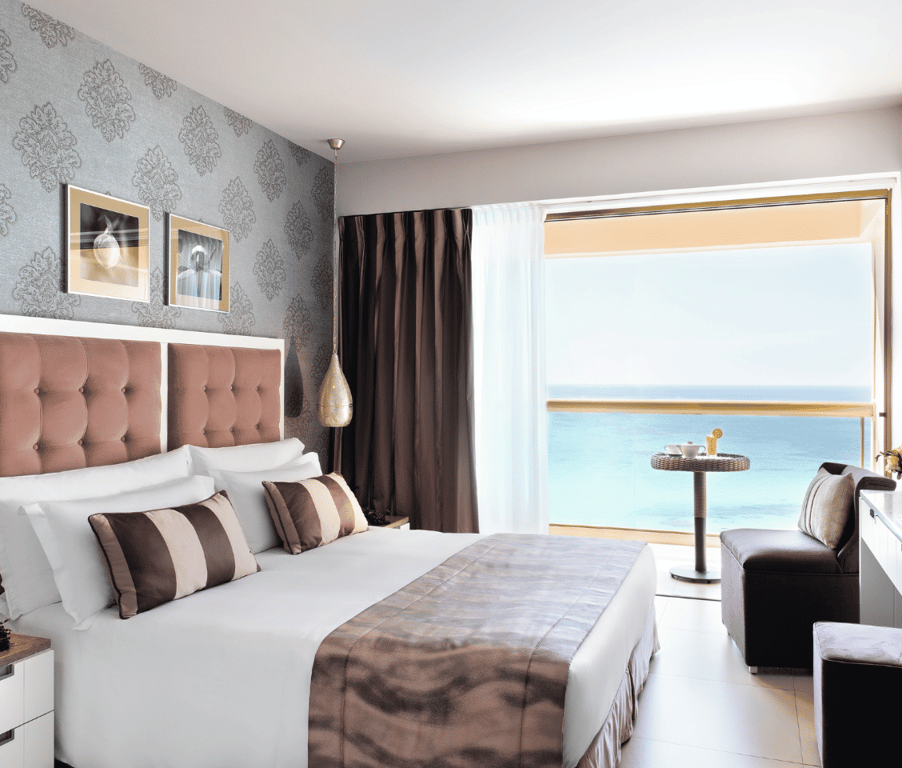 Luxurious Junior Twin Room at Sani Beach with two single beds, elegant décor, and stunning sea view from a large window.