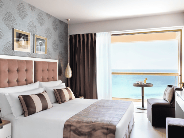 Luxurious Junior Twin Room at Sani Beach with two single beds, elegant décor, and stunning sea view from a large window.