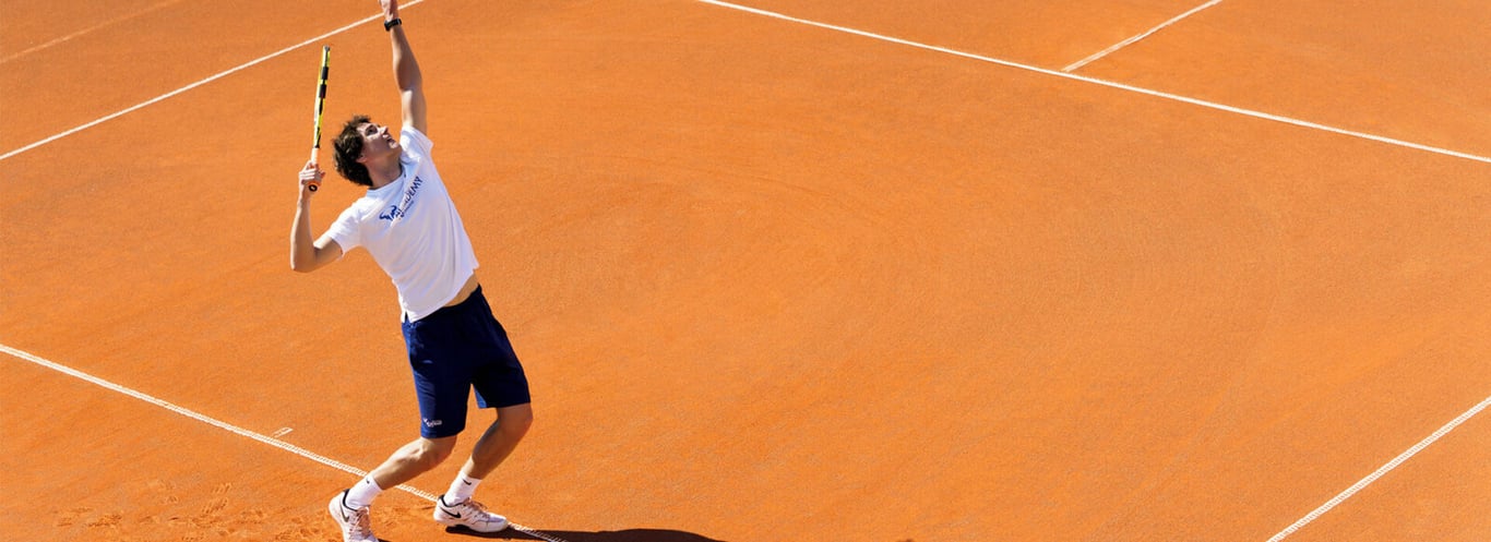 Tennis player serving on a clay court at Sani Beach, reflecting athletic grace and skill in a picturesque setting.