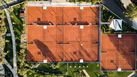 Aerial view of six clay tennis courts at Sani Beach resort, Greece, surrounded by greenery and pathways.