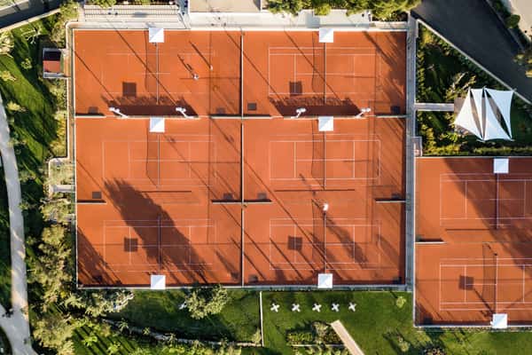 Aerial view of six clay tennis courts at Sani Beach resort, Greece, surrounded by greenery and pathways.