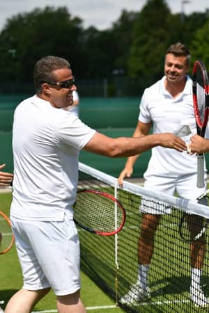 Four men in white tennis outfits shaking hands over the net on a grass court at St Georges Hill, showcasing sportsmanship.