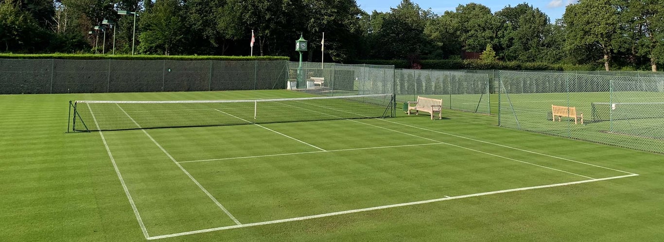 Pristine grass tennis courts at St George's Hill with surrounding greenery and blue sky.
