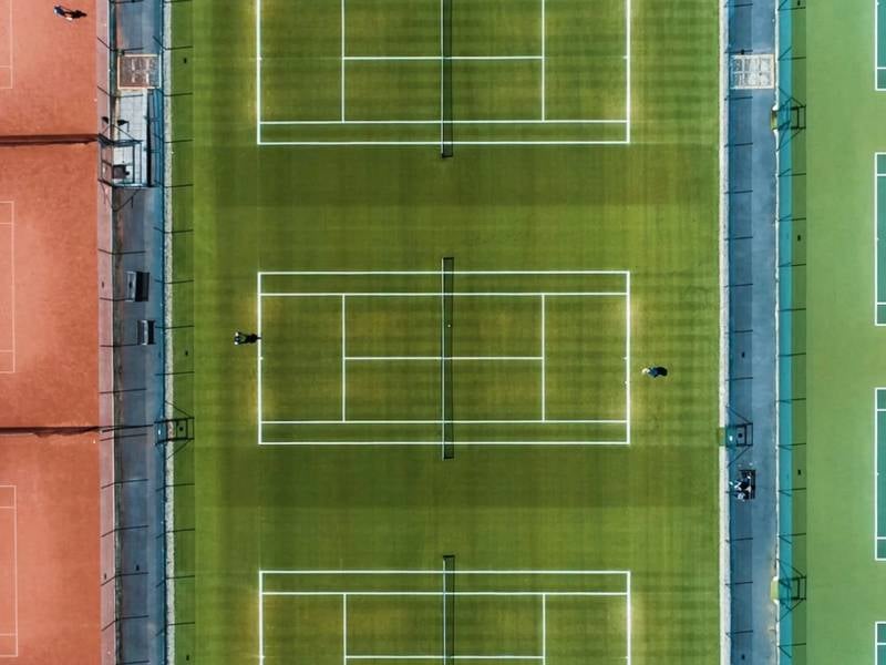 Aerial view of tennis courts at The Lensbury, showing two green courts and a clay court with clear white boundary lines.
