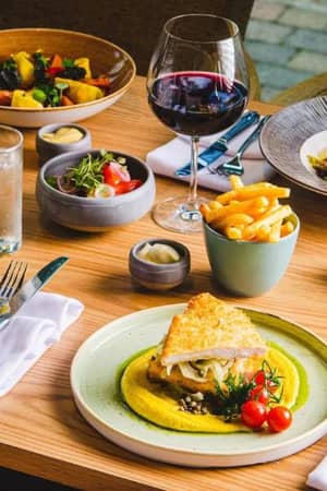 Dining table at The Lensbury featuring gourmet dishes such as roasted chicken, pasta, salad, and wine.