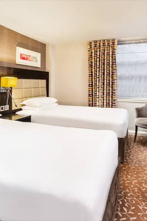 Cosy Lensbury Twin Room with two single beds, a bedside table, flat-screen TV, and patterned curtains.