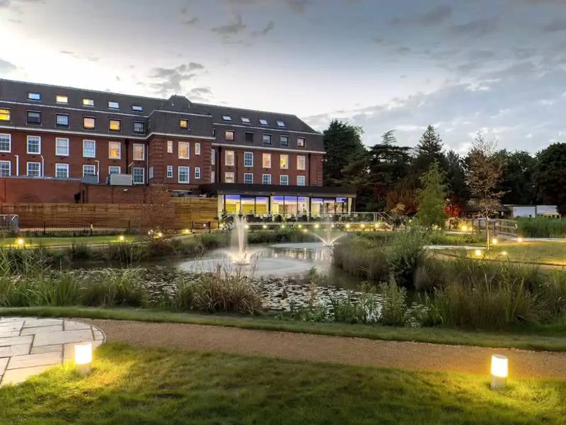 The Lensbury Hotel by the River Thames, showcasing landscaped gardens, a reflective pond, and evening lighting.