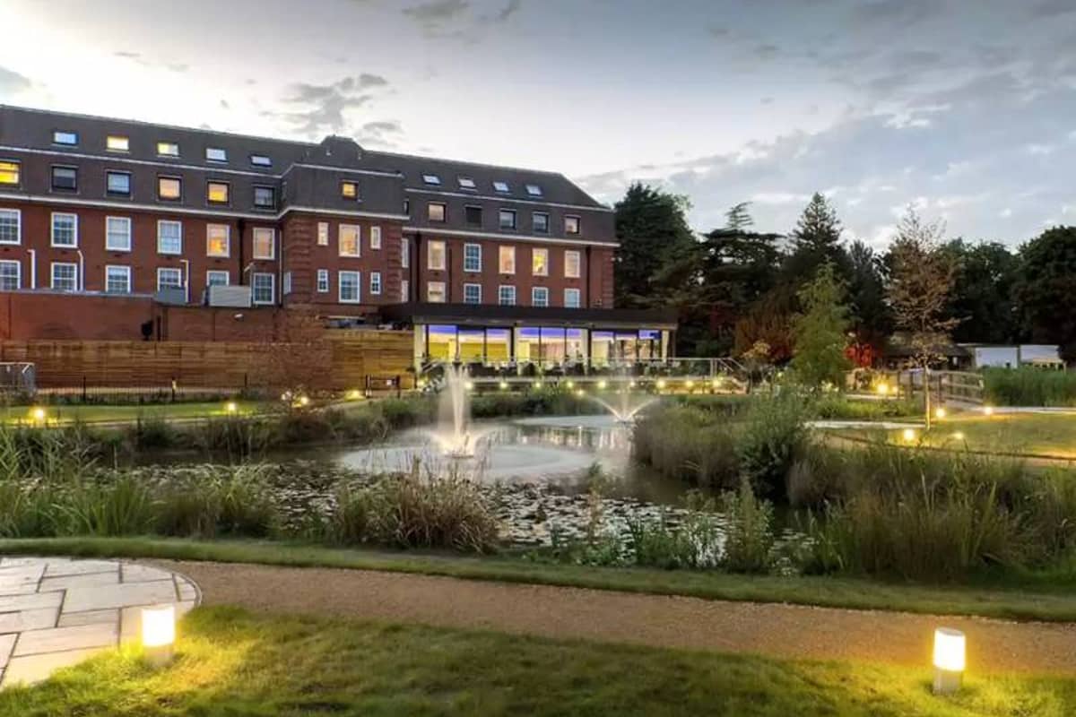 The Lensbury Hotel by the River Thames, showcasing landscaped gardens, a reflective pond, and evening lighting.