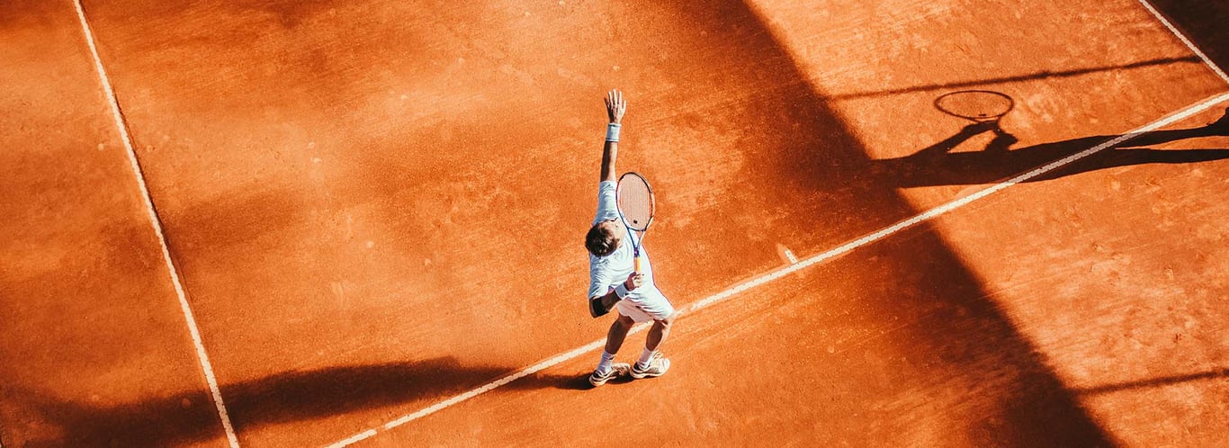 Tennis player preparing to serve on a clay court, emphasizing mental focus and strategy.