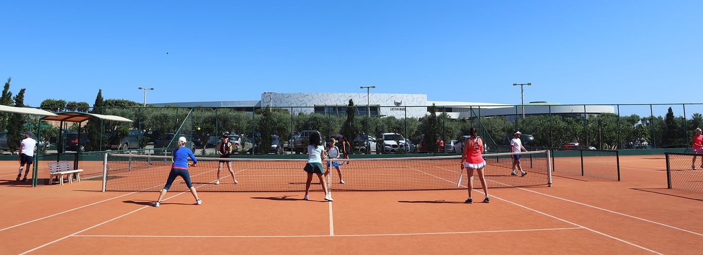 Players on a tennis court during the 2024 tennis holiday season, playing doubles matches with a modern facility in the background.