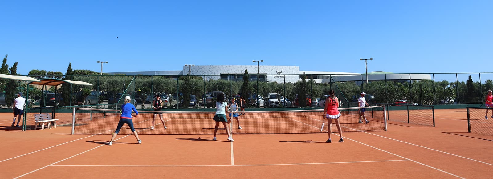 Players on a tennis court during the 2024 tennis holiday season, playing doubles matches with a modern facility in the background.