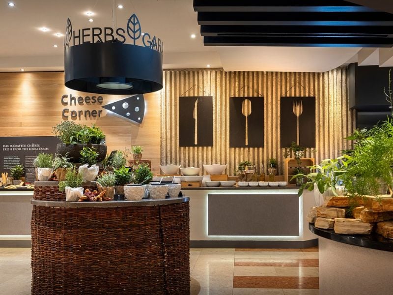 Dining area at Valamar with a Herb Garden, Cheese Corner, and wall art featuring forks, surrounded by plants and cheese selections.