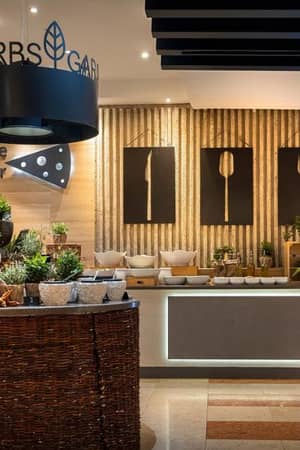 Dining area at Valamar with a Herb Garden, Cheese Corner, and wall art featuring forks, surrounded by plants and cheese selections.