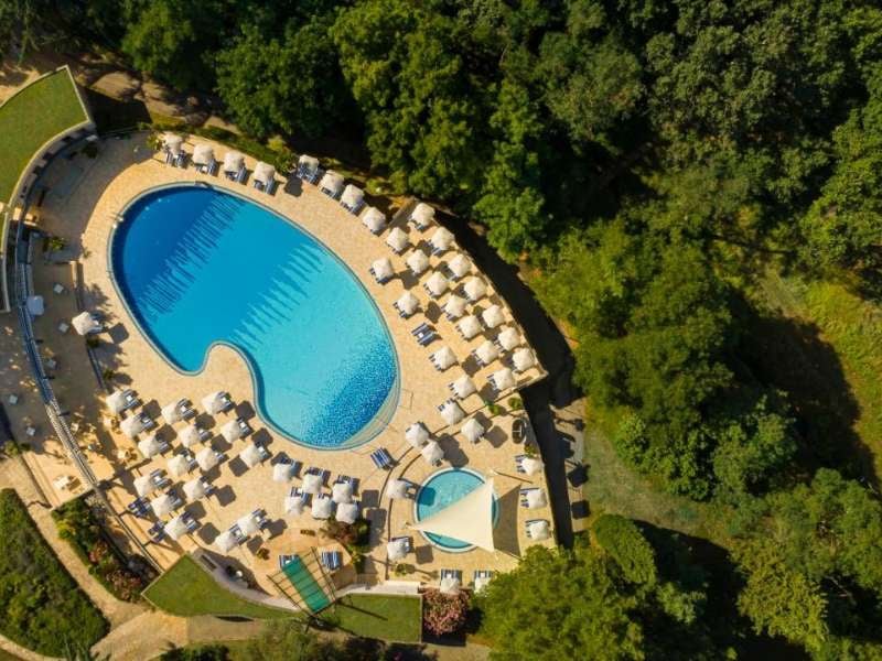 Overhead view of Valamar resort pool area, showing a large pool, many sun loungers, umbrellas, and surrounding greenery.