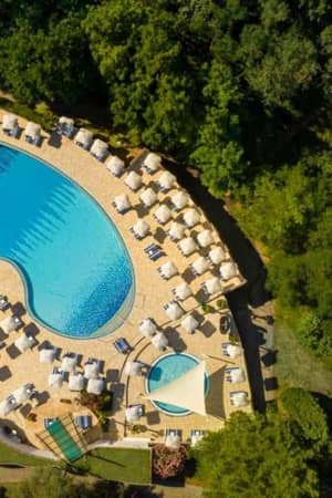 Overhead view of Valamar resort pool area, showing a large pool, many sun loungers, umbrellas, and surrounding greenery.