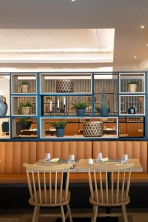 Interior of a Valamar Gallery restaurant with wooden seating, orange leather upholstery, and shelves with plants and vases.