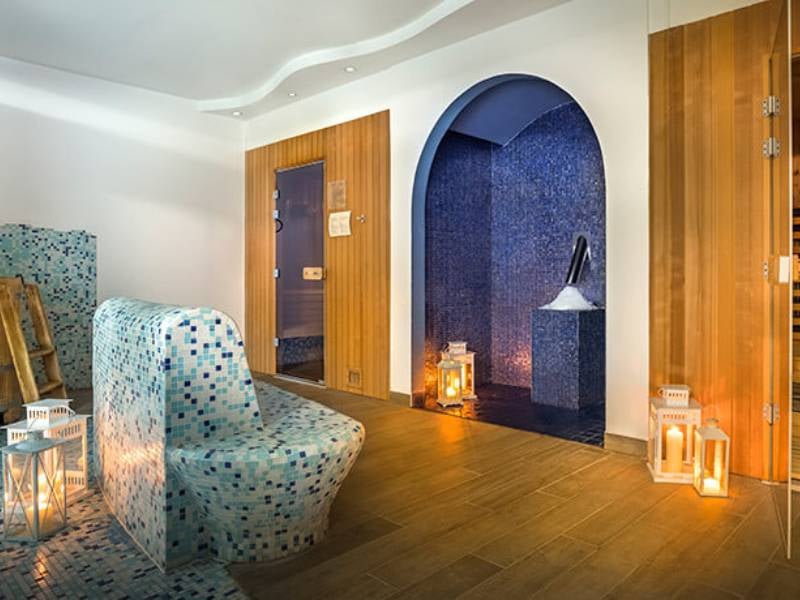 Luxurious spa room with mosaic-tiled steam room, contoured seating, wood panelled walls, and decorative lanterns.