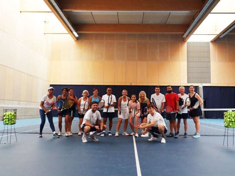 Group of 16 people with tennis rackets on an indoor court at Virgin Active Chiswick.