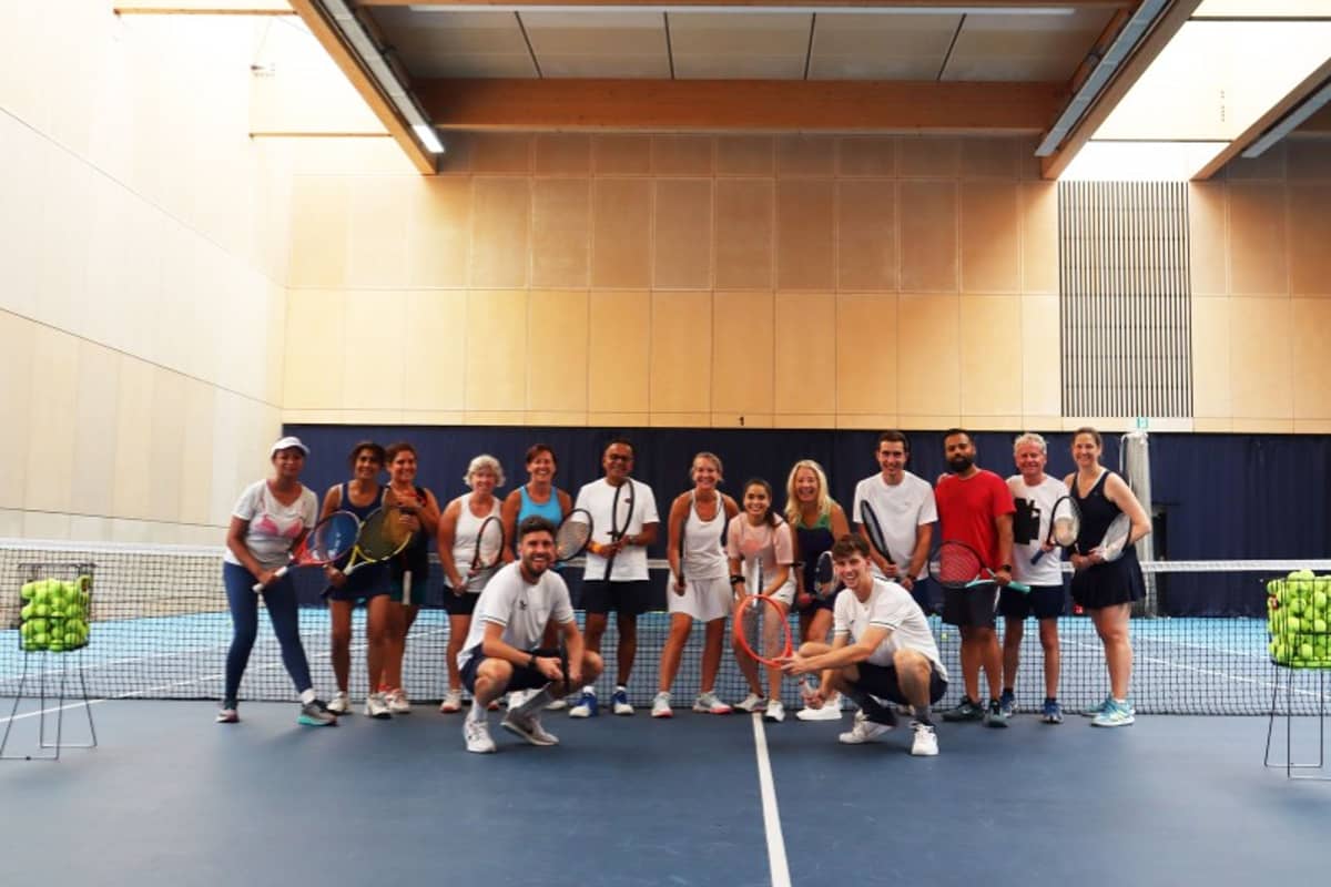 Group of 16 people with tennis rackets on an indoor court at Virgin Active Chiswick.