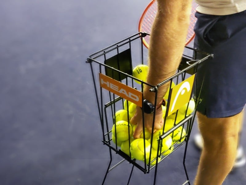 Close-up of a tennis ball basket with HEAD branding at Virgin Active Chiswick, on an indoor court.