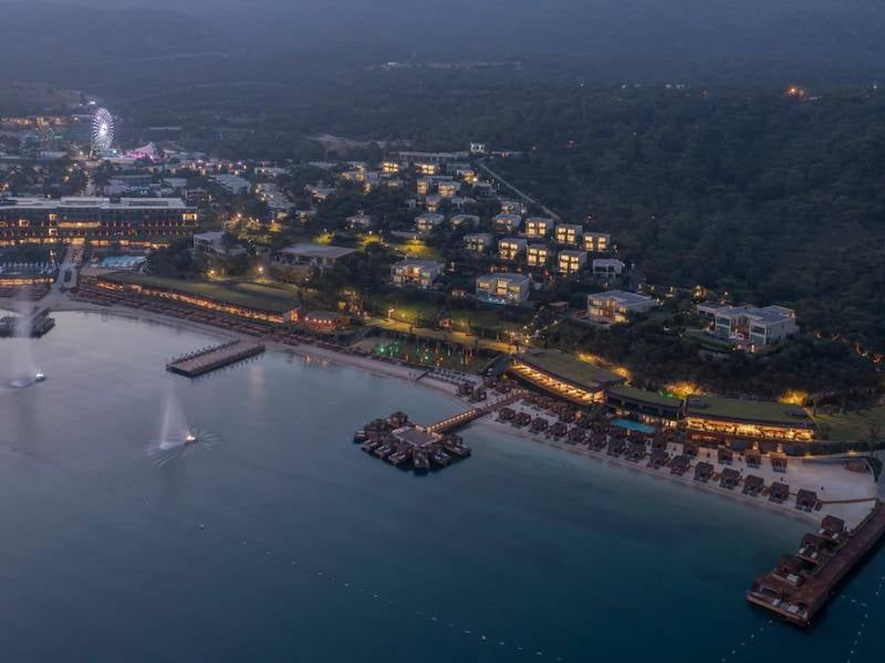 Aerial view of a seaside resort with beachfront villas and private decks over the water, surrounded by lush greenery at dusk.