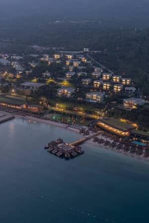 Aerial view of a seaside resort with beachfront villas and private decks over the water, surrounded by lush greenery at dusk.