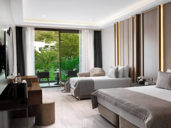 Vogue Superior Room interior with two beds, a work desk, TV, a seating area, and terrace access overlooking greenery.