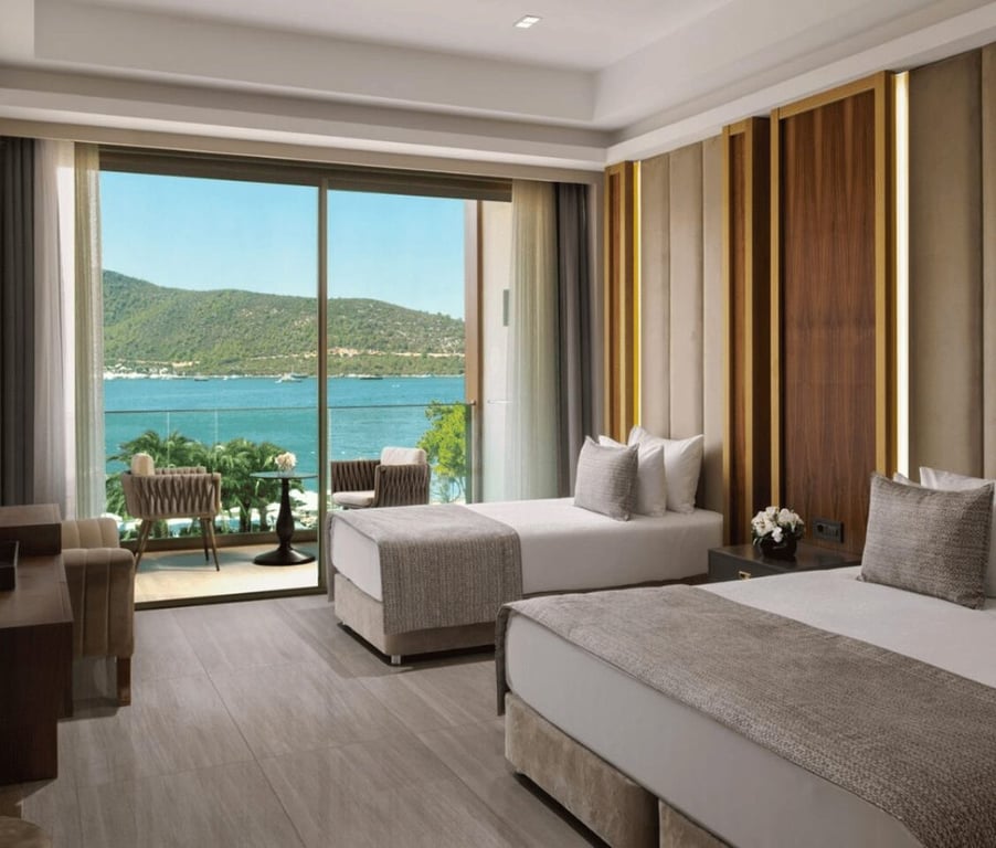 Vogue Superior Room with two twin beds, offering a sea view through floor-to-ceiling windows and a balcony, decorated in soft neutrals with wood accents.