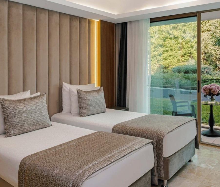 Twin beds in a modern garden room annex with outdoor seating access and garden views through large glass doors.