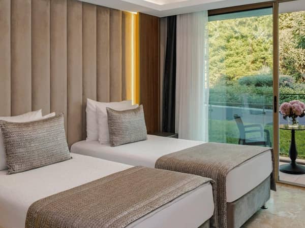 Twin beds in a modern garden room annex with outdoor seating access and garden views through large glass doors.