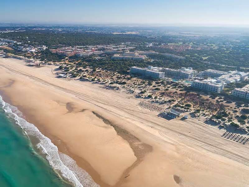 Aerial view showcasing Barosa Park Hotel, pristine beach, turquoise sea, and organized sun loungers, surrounded by lush greenery.