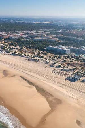 Aerial view showcasing Barosa Park Hotel, pristine beach, turquoise sea, and organized sun loungers, surrounded by lush greenery.
